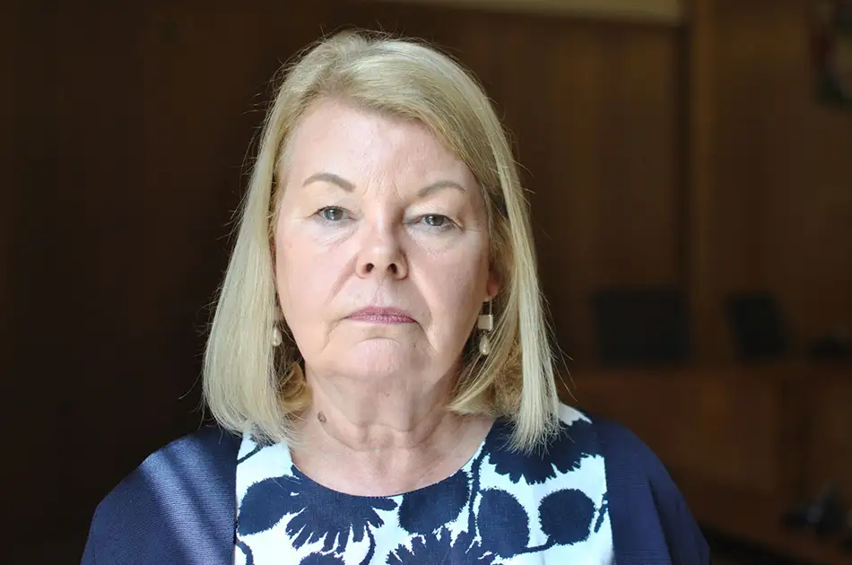 A woman with straight blonde hair and light skin, wearing a navy and white floral top, looks directly at the camera with a neutral expression. The softly lit background hints at local government reorganisation in Hampshire unitary councils.
