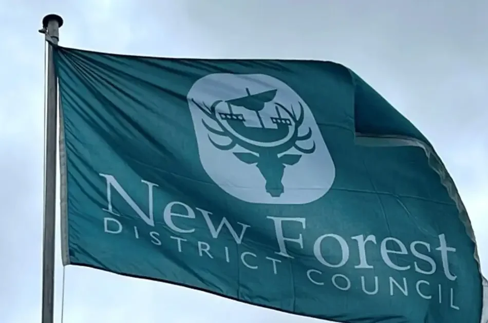 A teal flag with the white logo and text New Forest District Council flying on a pole.